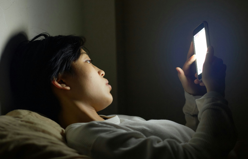 Woman scrolling on cell phone at night by Seth Bingham