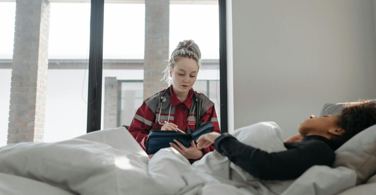 A healthcare worker takes notes while attending to a patient in bed providing home healthcare