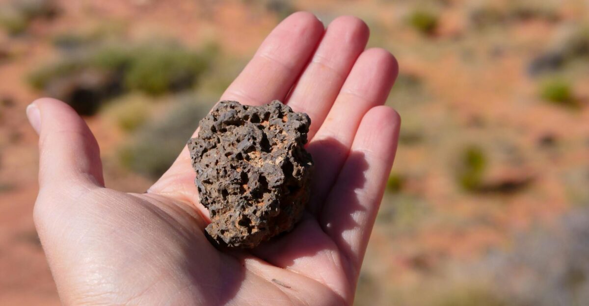 A close-up of a hand holding a rough volcanic stone in a desert landscape
